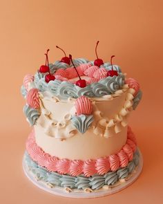 a three tiered cake with cherries on top and frosting in pastel colors