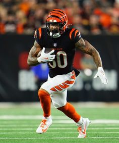 a football player running with the ball in his hand and wearing an orange helmet on