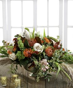 a vase filled with lots of flowers sitting on top of a wooden table next to candles