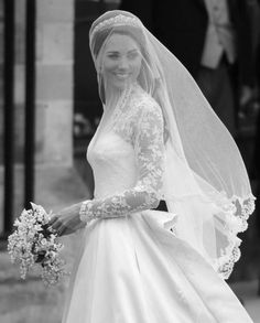 the bride is walking down the street in her wedding dress and veil with flowers on it