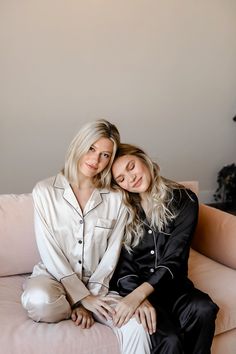 two women sitting on top of a pink couch next to each other, both wearing pajamas