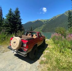 a red pick up truck parked on the side of a road next to a lake