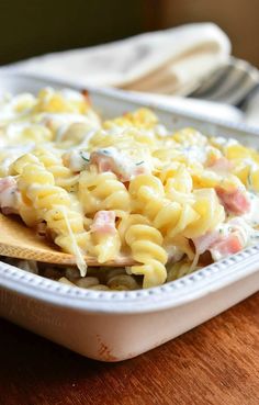 a wooden spoon filled with macaroni and cheese on top of a white dish