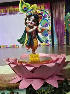 a small statue is on display in front of a stage with pink flowers and green leaves