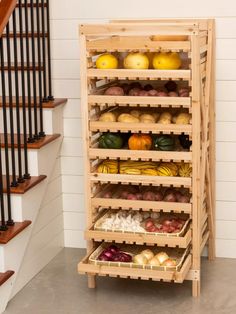 a wooden rack filled with fruits and vegetables next to a stair case in a house