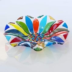 a multicolored flower brooch sitting on top of a white table next to a glass vase