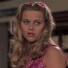 a woman with blonde hair and blue eyes in a pink dress looking at the camera