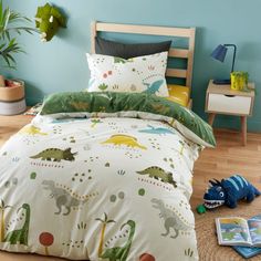 a child's bedroom with dinosaur bedding and toy dinosaurs on the floor next to it