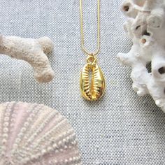 We love this fun and summery, beachy necklace. Answer the siren's song and get one for yourself or someone you love. Would make a great gift for the surfer or beach-lover in your life! A 14k gold electroplated cowrie shell dangles from a lustrous, high quality gold filled snake chain. The perfect summertime accessory! Chain: Gold fill, length 16" Cowrie Pendant: 22k Gold plated size: 26 x 18 mm✦ JEWELRY CARE ✦✧ Warm water and a soft cloth are the best thing you can do to maintain the beauty of y Gold Cowrie Shell As Gift, Gold Cowrie Shell Jewelry For Gift, Ocean-inspired Necklaces For Summer Gifts, Ocean-inspired Necklaces As Summer Gifts, Handmade Gold Shell Strand, Handmade Gold Strand Shell, Beach Jewelry With Charms In Ocean-inspired Style, Charm Jewelry For Beach, Ocean-inspired Jewelry With Charms For Beach