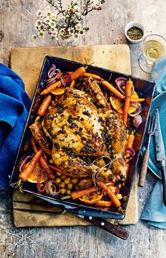 a roasting pan filled with chicken, carrots and onions on a wooden table