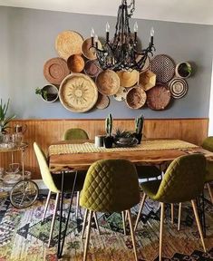 a dining room table with green chairs and baskets on the wall above it, in front of a chandelier