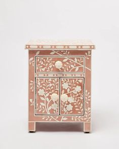 a pink and white painted wooden cabinet with flowers on it's side drawer, against a white background