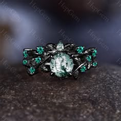 a ring with green and white stones on it sitting on a stone surface, in front of the camera