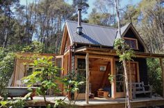 a small wooden cabin in the woods surrounded by trees and shrubs, with a hot tub on the deck