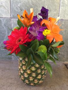 a pineapple vase filled with colorful flowers and greenery on top of a counter