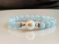 Bring the ocean to you with this beautiful aquamarine and shell pearl bracelet. These all-natural aquamarine cool blue beads have a soft, almost organic feel to them. At the center is a large 14mm natural shell pearl which makes this bracelet "Pop". Choose your aquamarine bead size, available in 10mm or 12mm aquamarine beads. Made with high-quality stretch cord for convenience and comfort.  Choose your wrist size for a more personalized fit.   Aquamarine, the gemstone of tranquility and clarity, March Bracelet, Aquamarine Bracelet Beads, Aquamarine Bracelet, Aquamarine Beads, Bright Star, Birthstone Bracelet, March Birthstone, Birthstone Bracelets, Aquamarine Gemstone