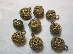 nine antique brass plated beads on a white tablecloth, some with holes in them