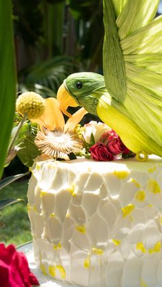 two birds on top of a white cake with yellow and red flowers in the background