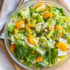 a salad with oranges and lettuce in a glass bowl on a wooden cutting board