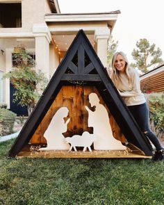 a woman standing next to a nativity scene in front of a house with christmas lights