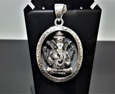 a silver pendant with an image of the god ganesh in a round frame on a black stand