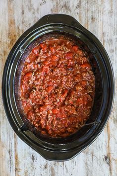 a crock pot filled with chili on top of a wooden table