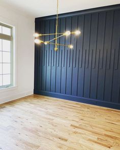 an empty room with wood flooring and blue paneled wall behind the chandelier