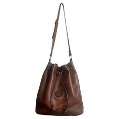 Very pretty Longchamp shoulder bucket bag in brown grained leather. The bag has a leather drawstring to open and close it. The Longchamp leather logo is present on the front of the bag. The gold metal parts are stamped Longchamp Paris. This bag is a magnificent vintage model from the famous French house Longchamp. The leather is beautiful and of high quality. The interior has pockets. This bag combines authenticity and elegance. The leatherwork is magnificent. Genuine Signature leather at Longchamp from the 70s, it can be found on lines of luggage and handbags with a refined design in the leather goods tradition of the House. This bag is a wonderful classic, vintage and timeless. Magnificent color and material. Note some cracks on the inside, invisible when the bag is worn. Longchamp's suc Brown Smooth Grain Bucket Bag, Textured Leather Bucket Bag For Travel, Formal Brown Bucket Bag, Cognac Textured Leather Bucket Bag, Classic Leather-lined Bucket Bag, Classic Bucket Bag With Leather Lining, Classic Brown Soft Leather Bucket Bag, Travel Bucket Bag In Textured Cognac Leather, Classic Brown Textured Leather Bucket Bag