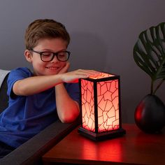 a young boy sitting on a couch next to a table with a lamp in front of him