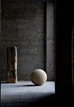 a white ball sitting on top of a cement floor next to a tall brick pillar