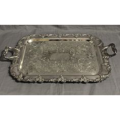 an ornate silver tray with handles and flowers on the bottom, sitting on a tablecloth