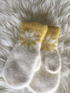 two white and yellow mittens laying on top of a furry surface