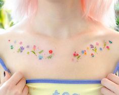 a woman with pink hair and tattoos on her chest holding onto a yellow top that has flowers all over it