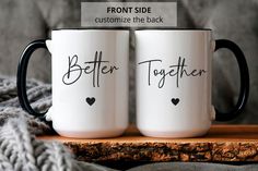 two coffee mugs sitting on top of a wooden table next to a gray blanket