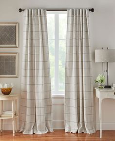 a living room with white walls and wooden flooring, two windows covered in beige plaid curtains