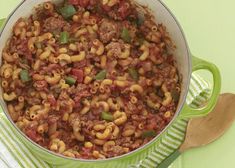 a green pot filled with pasta and meat on top of a table next to a wooden spoon