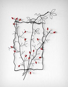 a wire sculpture with red berries hanging from it's sides on a white wall