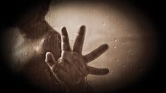 a person's hand reaching out from behind a rain covered glass window with drops of water on it