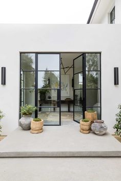 an entrance to a white house with glass doors and potted plants on the steps