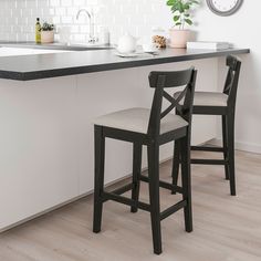 two stools in front of a counter with a clock on the wall above it