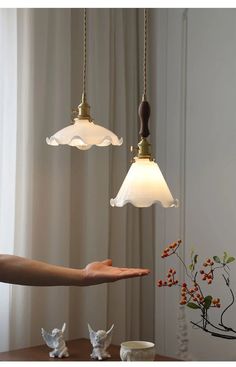 a person holding out their hand in front of two hanging lights that are white and gold