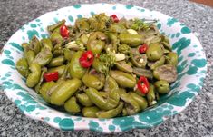 a bowl filled with green beans and red peppers on top of a granite countertop