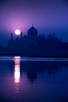 the sun is setting over an old building on the water with its reflection in the water