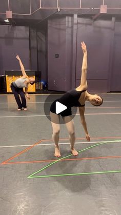 two women doing yoga exercises in an indoor gym area with colored lines on the floor