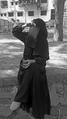 a woman wearing a hijab is sitting on the steps and eating something in her hand