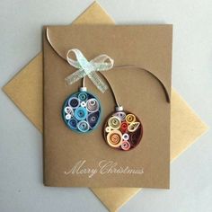 a christmas card with two ornaments hanging from it's side on top of a brown envelope