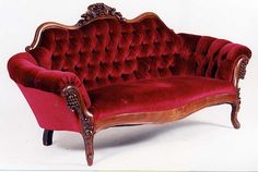 a red velvet couch sitting on top of a white floor next to a wooden frame