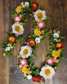 the letter o made out of flowers on a wooden floor with greenery around it