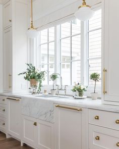 a kitchen with white cabinets and marble counter tops, gold pulls on the handles, and brass knobs