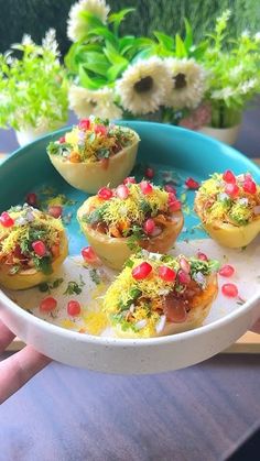 a person holding a blue plate with small food items on it and flowers in the background